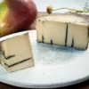 True blue vegan cheese by Mouse's Favourite segment of cut blue cheese in front to show blue veins - older style small round wheel