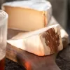 Beer washed rind vegan cheese by Mouse's Favourite cut slice showing spruce bark edge with glass of dark ale in foreground with an orange sunset hour glow.