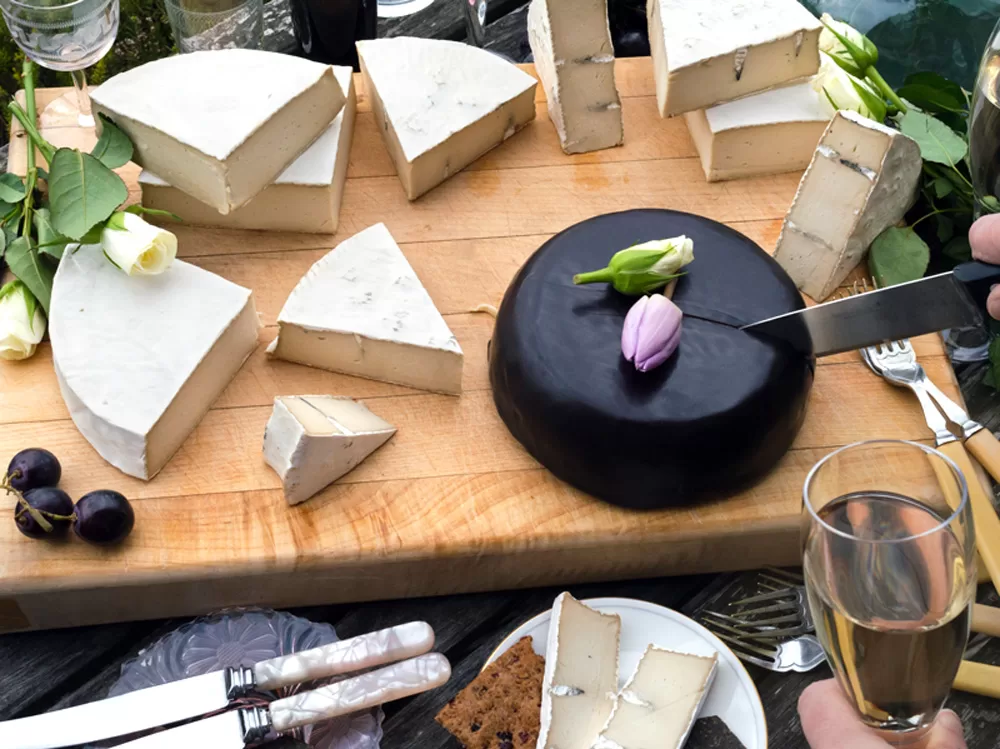 Special occasion vegan cheese by Mouse's Favourite - full large wheels of cheese layed out on cheeseboard ready for cutting. Camembert, camblue and aged classic with cut flower decorations.